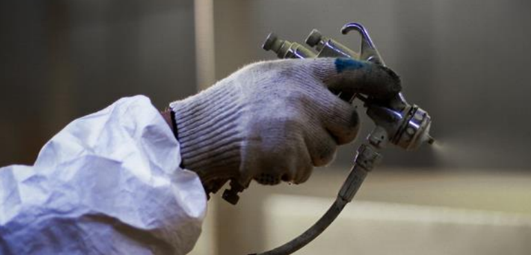 En hand i skyddskläder håller i ett sprutmunstycke för lackering