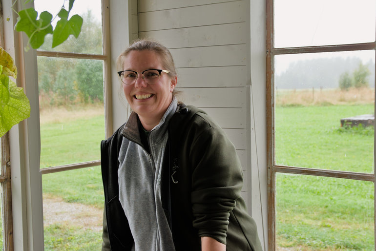 En kvinna med glasögon står framför ett fönster