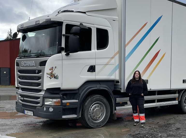 En kvinna står framför en lastbil från Sollefteå gymnasium uppställd på en grusplan.