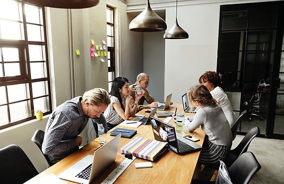 Fem personer arbetar tillsammans med sina datorer i ett grupprum